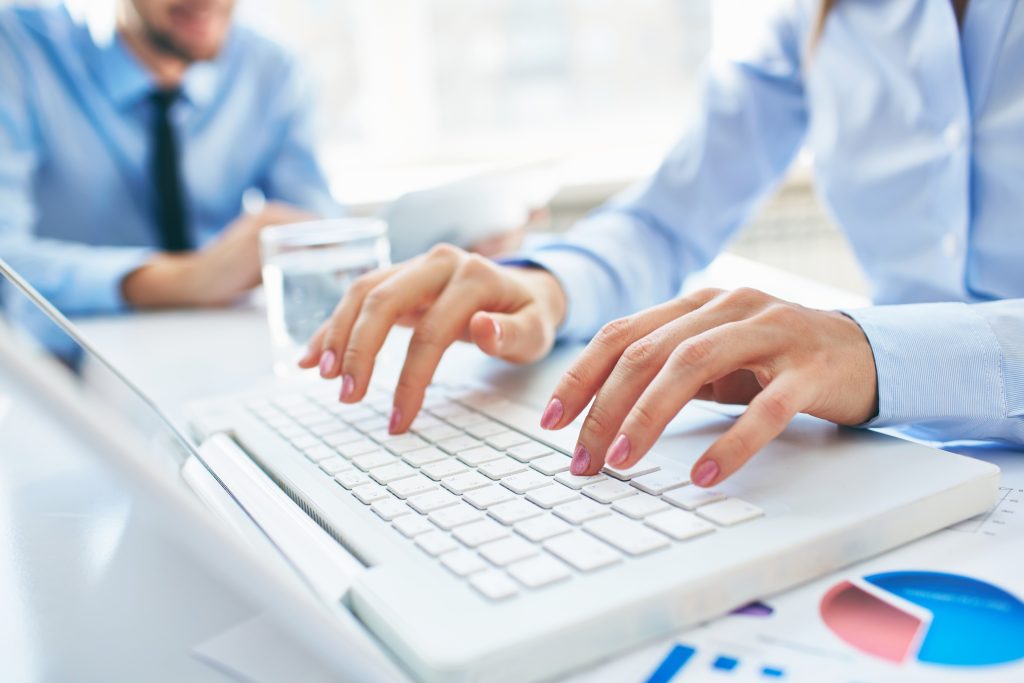 mãos femioninas digitando em um teclado branco de notebook.