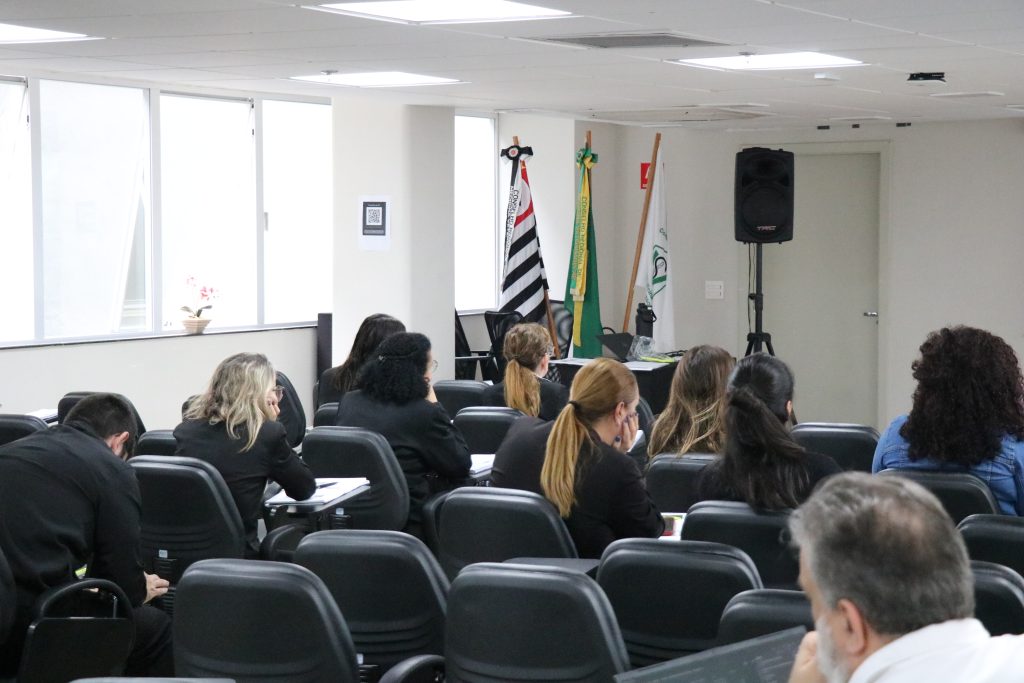 Pessoas de costas em auditório prestando atenção.