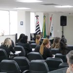 Pessoas de costas em auditório prestando atenção.