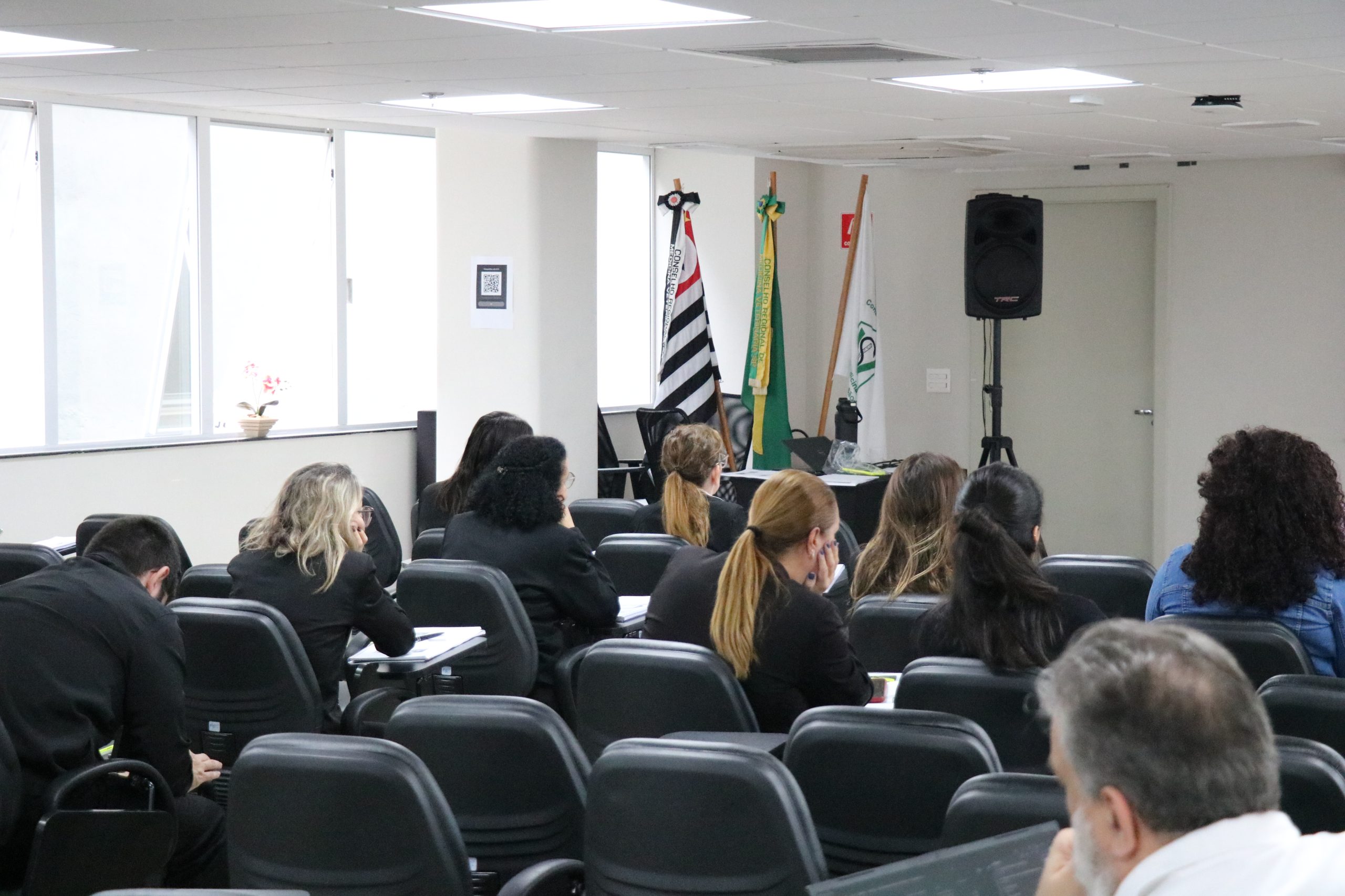 Pessoas de costas em auditório prestando atenção.