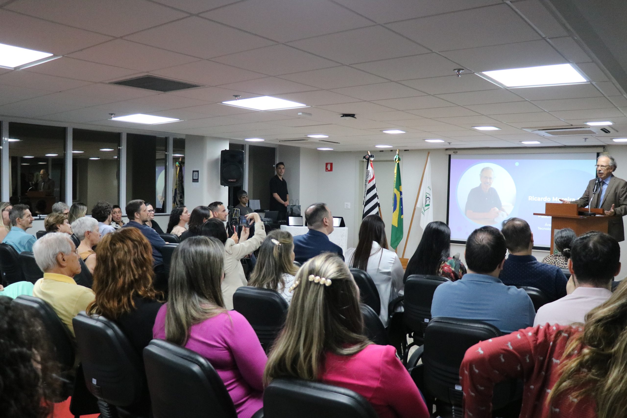 Com o auditório da sede lotado, ao fundo, no púlpito, o premiado discursa em agradecimento.