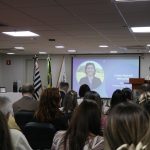 A premiada na categoria Pesquisa discursa no púlpito para auditório lotado, ao fundo sua foto aparece no telão.