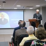 O premiado na categoria Zootecnia discursa aos presentes no auditório, ele está no púlpito e ao fundo sua foto aparece no telão.