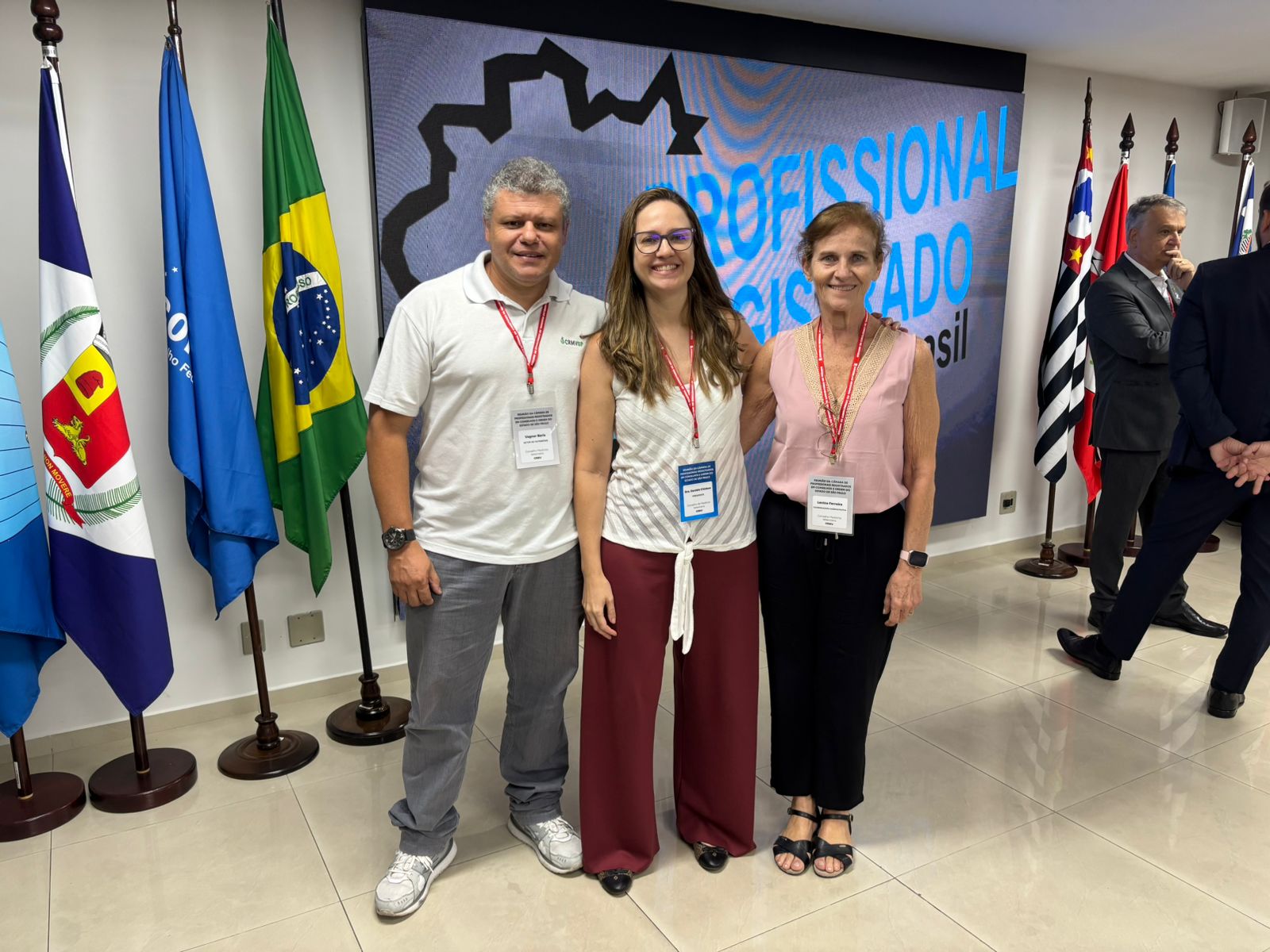 homem de camiseta branca posando para foto com 2 mulheres uma de branco e outra de rosa