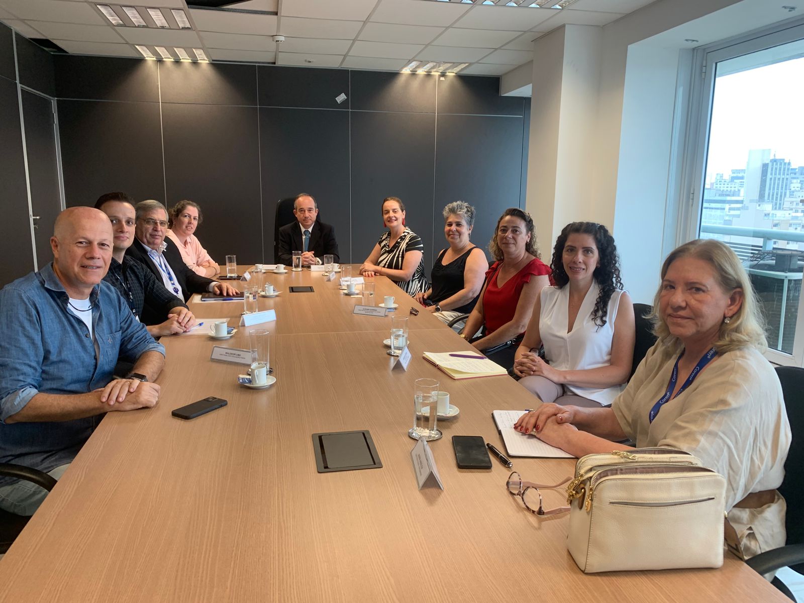 Pessoas sentadas em mesa sorrindo para foto em reunião co Procon.