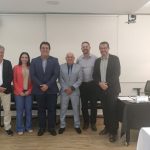 Seis pessoas em pé, cinco homens e uma mulher, lado a lado, pousando para foto em uma sala de escritório com cadeiras pretas, ar condicionado branco à esquerda, planta ornamental e parede branca ao fundo. À direita no fundo, uma mesa toalha preta, papéis, computador e dois copos de água, mais à frente, uma mesa com toalha branca. À esquerda, outra mesa com toalha preta. Entre os presentes, está a vice presidente do CRMV-SP, Carolina Saraiva Filippos de Toledo.