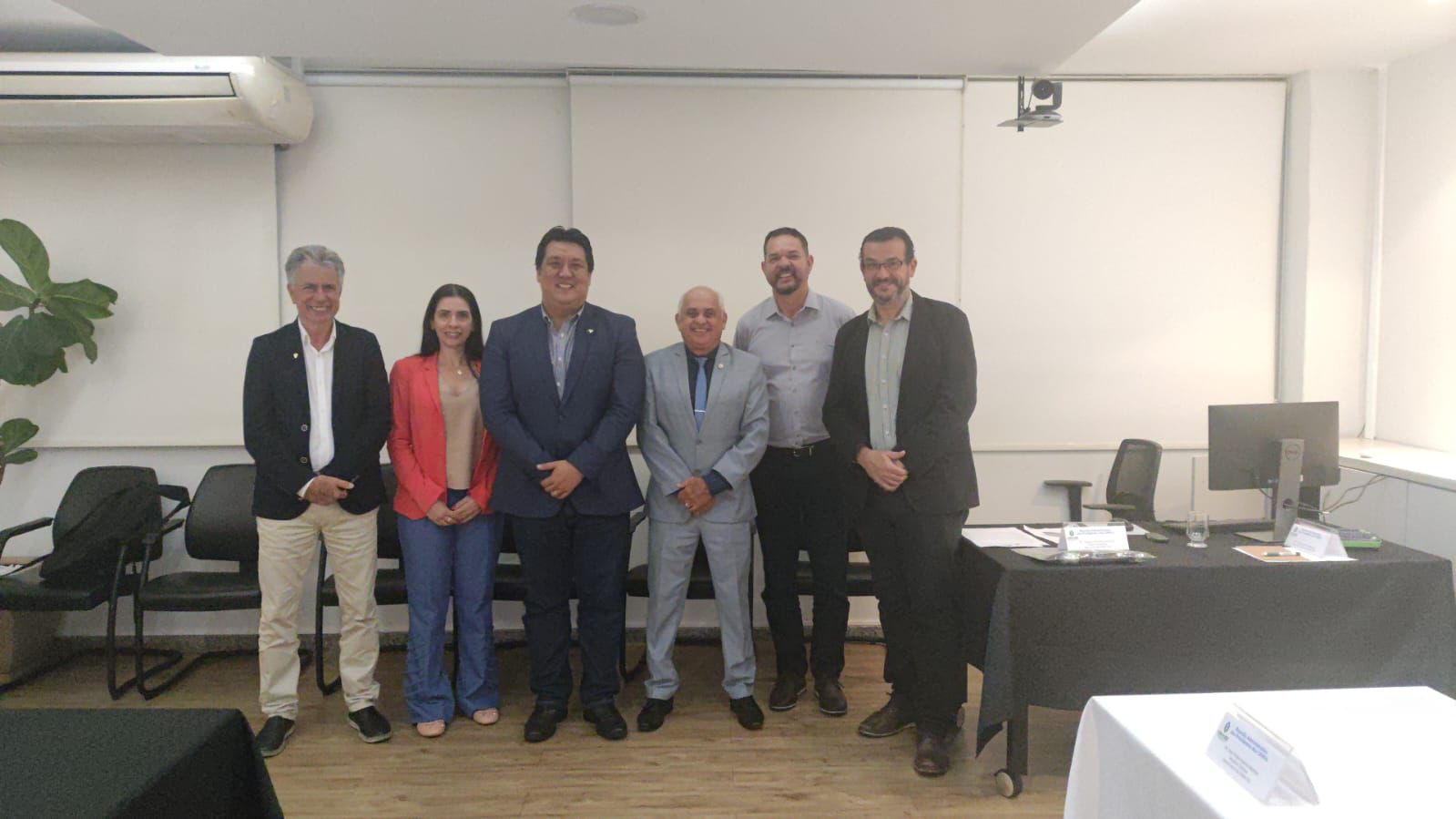Seis pessoas em pé, cinco homens e uma mulher, lado a lado, pousando para foto em uma sala de escritório com cadeiras pretas, ar condicionado branco à esquerda, planta ornamental e parede branca ao fundo. À direita no fundo, uma mesa toalha preta, papéis, computador e dois copos de água, mais à frente, uma mesa com toalha branca. À esquerda, outra mesa com toalha preta. Entre os presentes, está a vice presidente do CRMV-SP, Carolina Saraiva Filippos de Toledo.