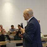 Homem careca, utilizando terno, palestrando.