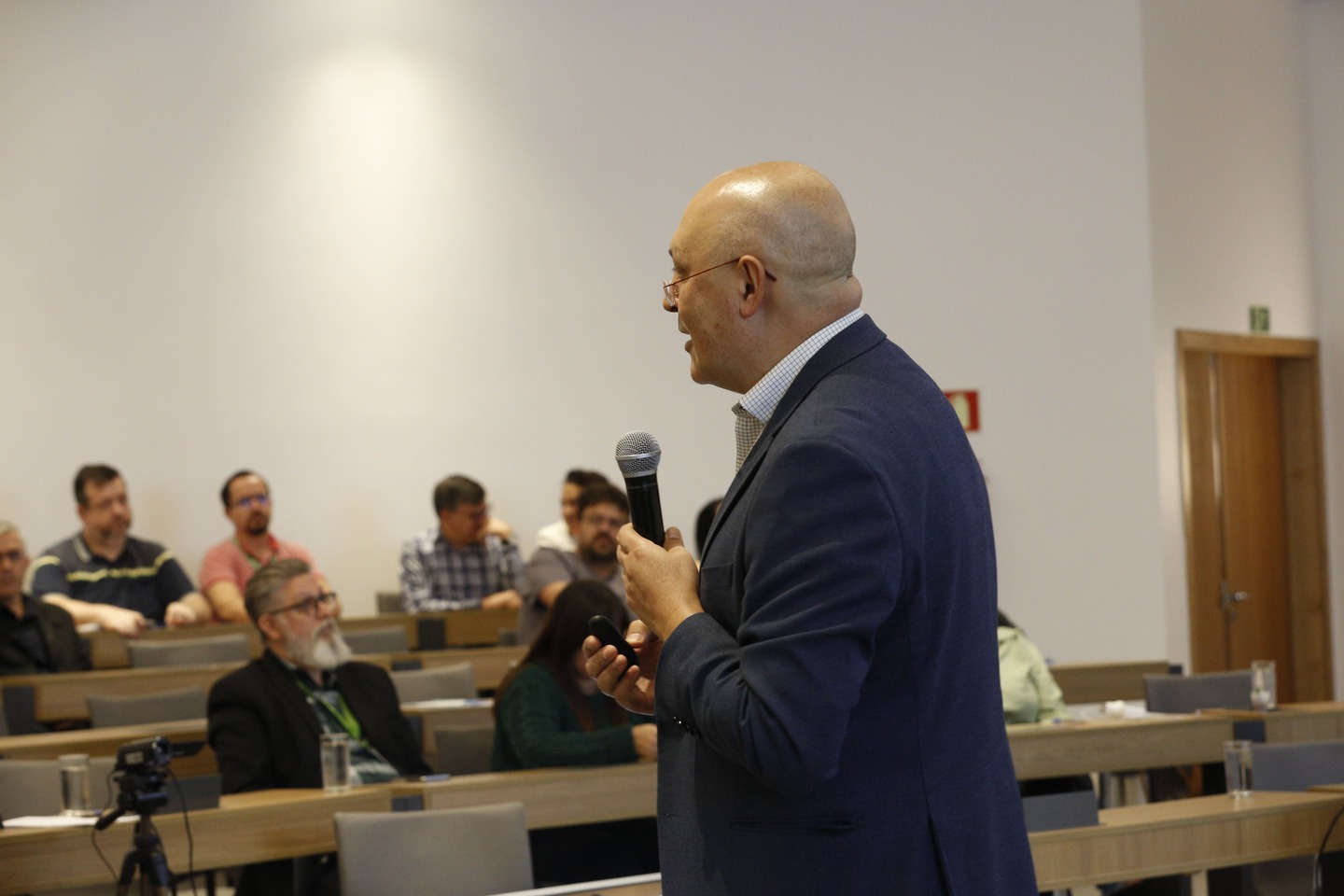Homem careca, utilizando terno, palestrando.