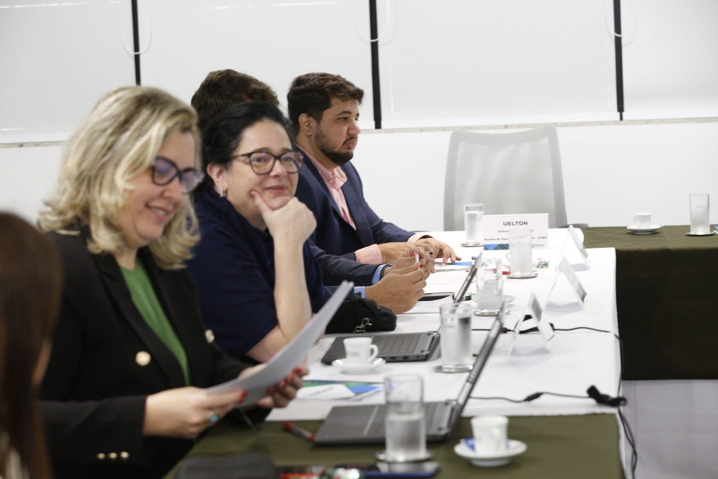 Duas mulheres e um homem sentados a uma mesa com computador para cada.