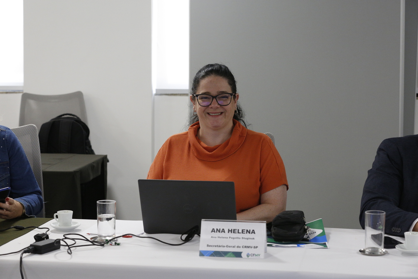 Uma mulher de pele branca, cabelo preto, camiseta laranja e utilizando óculos. Essa é a secretária geral do CRMV-SP Ana Helena Pagotto.