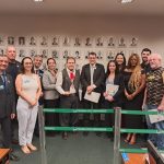 Pessoas em pé lado a lado, posando para foto com o deputado federal, Pompeo de Mattos.