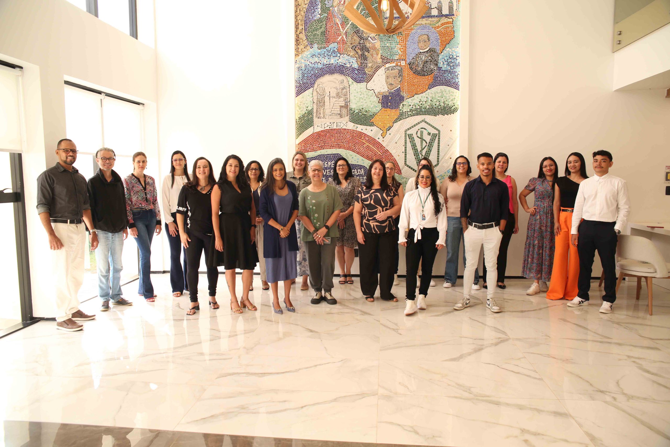 Homens e mulheres reunidos para foto. Ao fundo, uma obra de arte feita em azulejos.