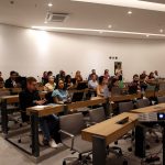 Visão lateral de todos os participantes do encontro sentados frente ao palco.