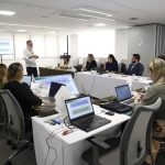Pessoas distribuídas na sala utilizando computador em reunião.