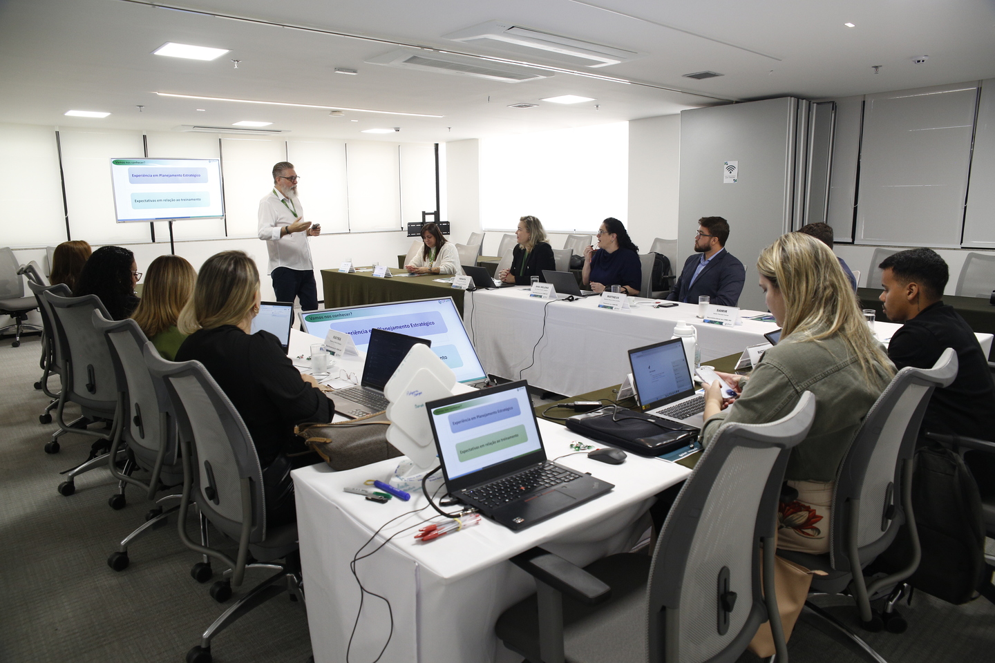 Pessoas distribuídas na sala utilizando computador em reunião.