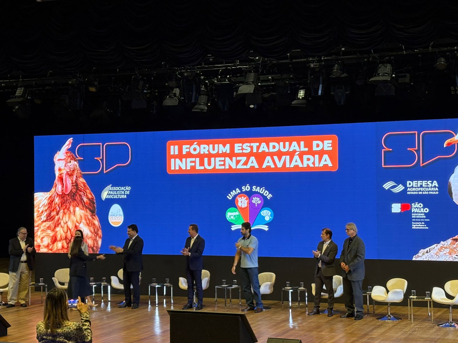 Pessoas reunidas no palco para apresentação durante segundo fórum estadual de influenza aviária..