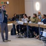 Homem palestrando a frente de participantes.