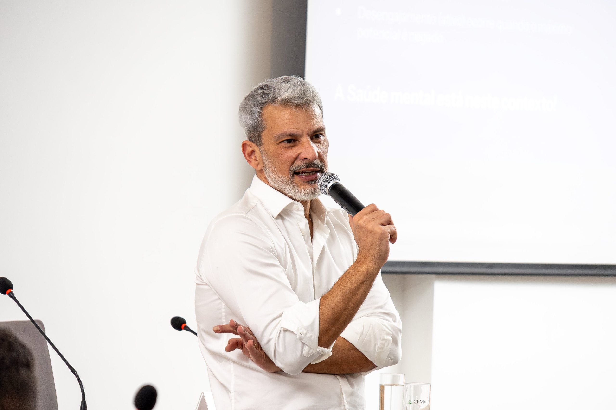 Homem de cabelo grisalho e camiseta branca falando ao microfone, Esse é o Daniel Costa, diretor executivo da Agência BWG.in