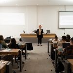 Mulher falando frente ao público sentado.