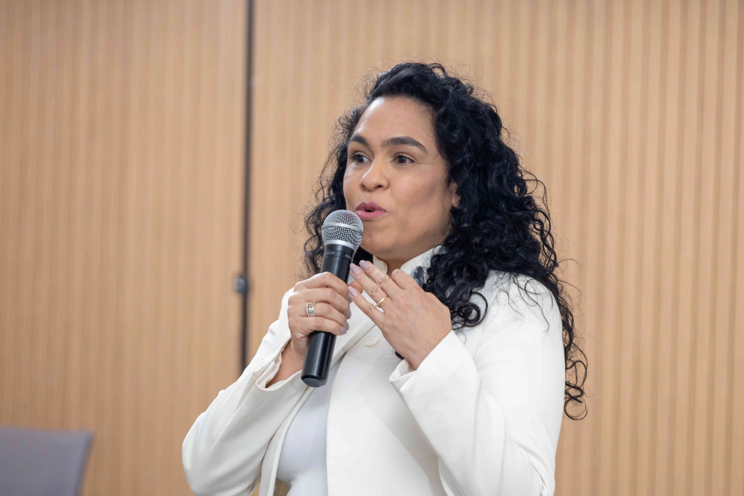 Mulher de cabelo preto e blusa branca falando ao microfone.