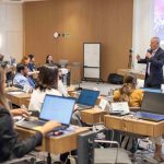 Homem grisalho falando ao microfone para o público.