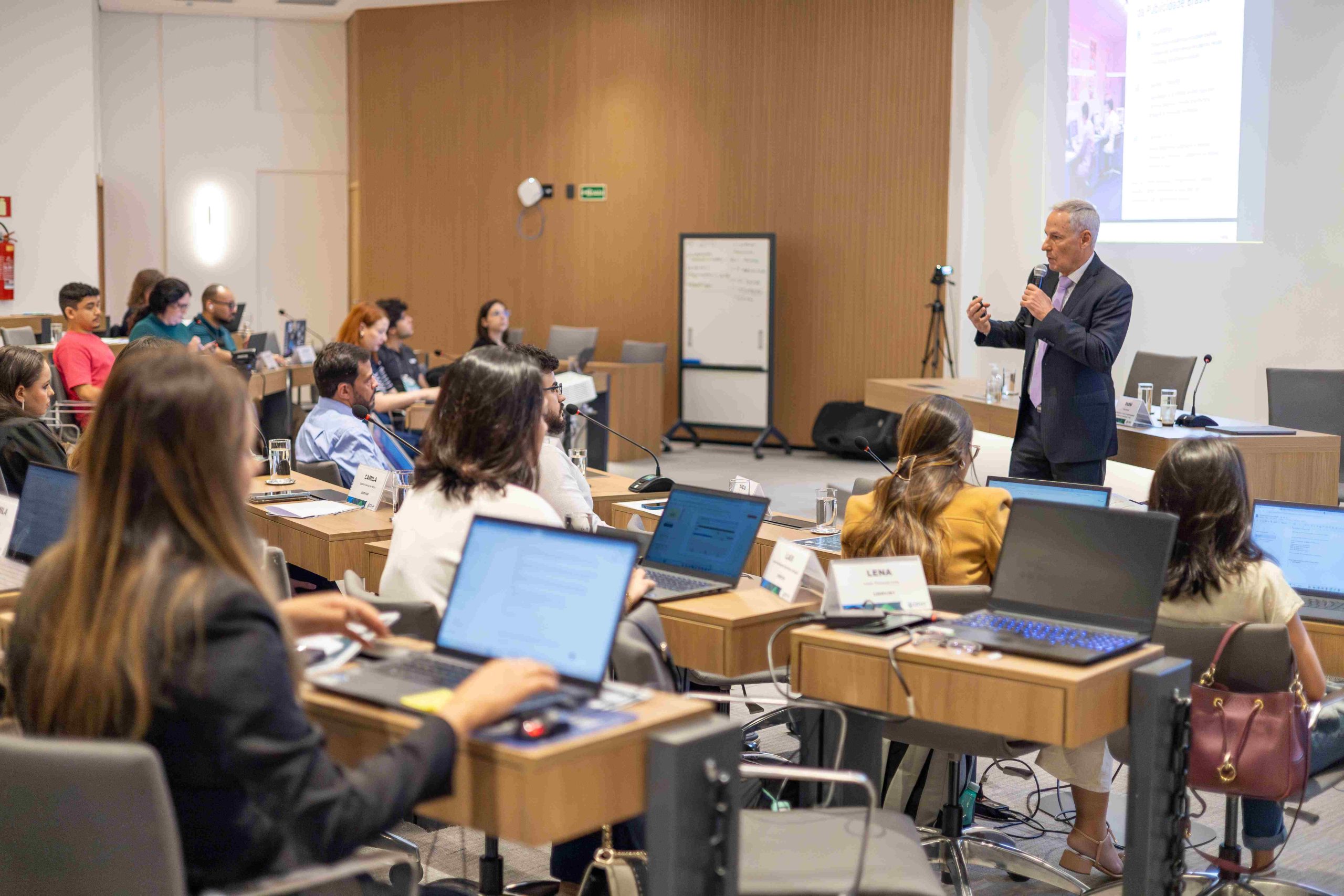 Homem grisalho falando ao microfone para o público.