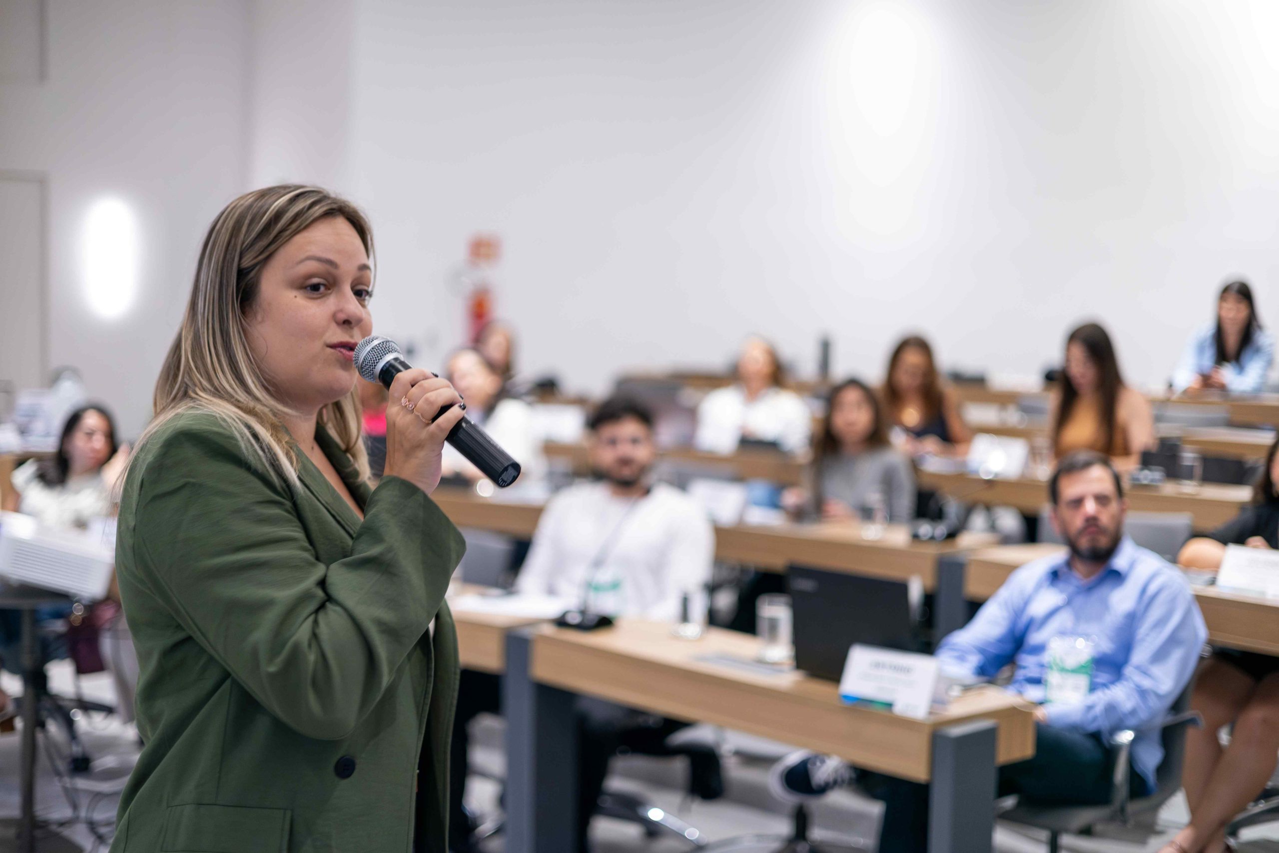 Mulher falando ao microfone para público.