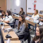 Pessoas sentadas a mesa olhando para o telão.