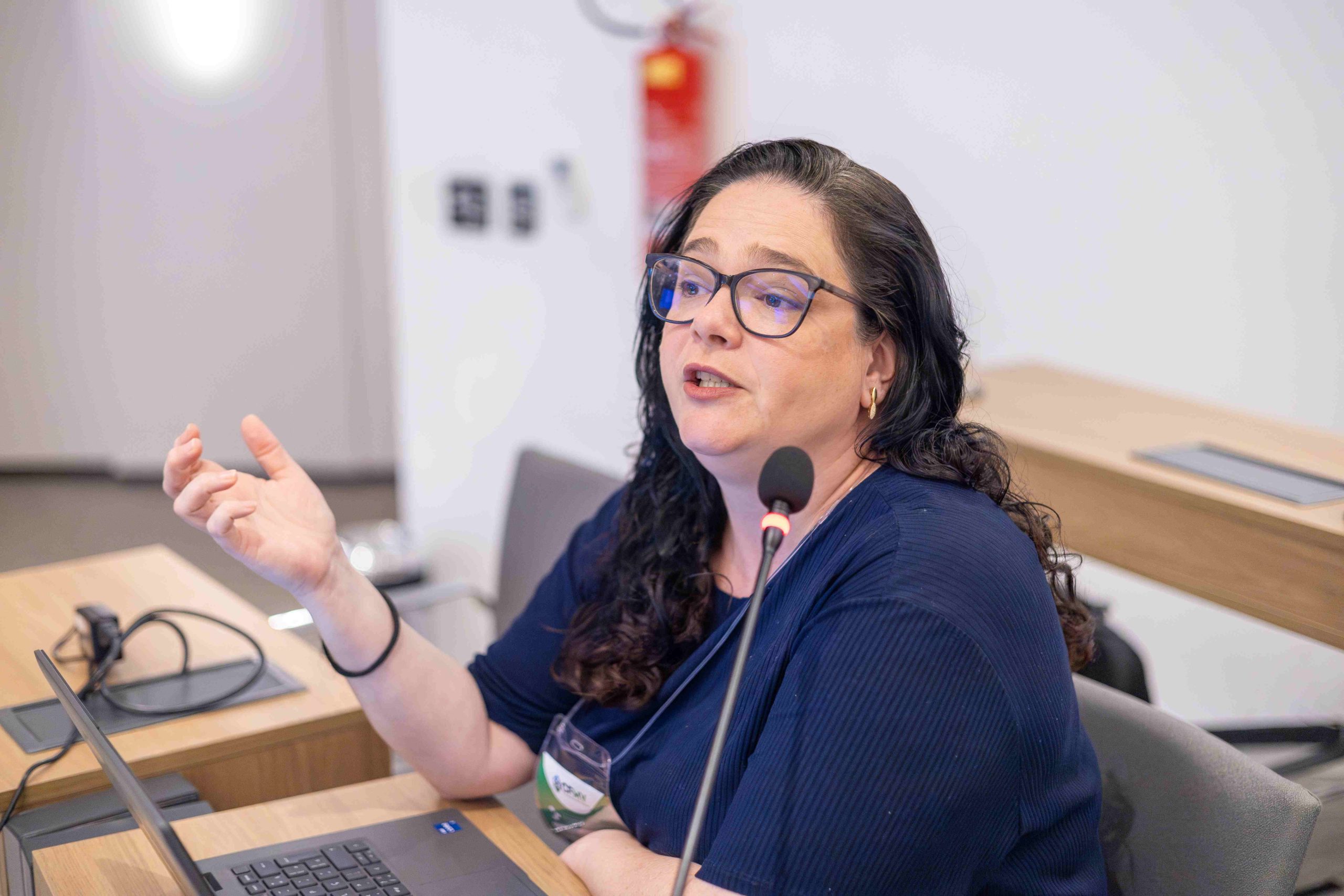 Na foto há uma mulher de cabelo pretos e longo, óculos e camiseta azul. É a dra. Ana Helena Pagotto.
