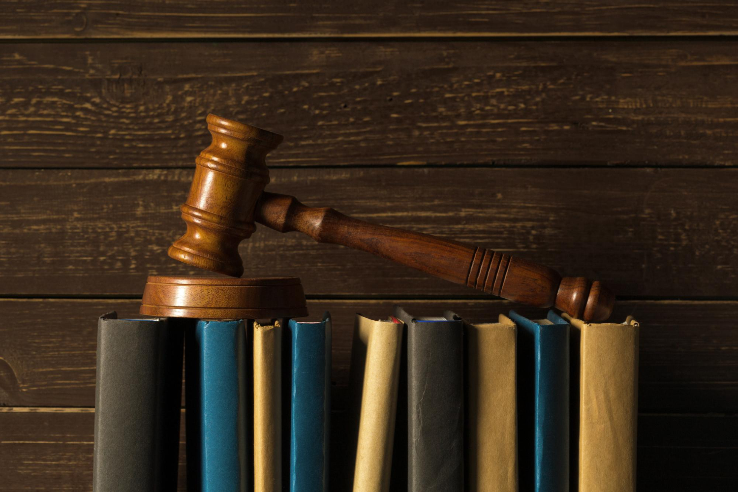 Martelo de madeira marrom utilizado comumente em tribunais deitado sobre livros e processos jurídicos.