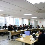 Pessoas sentadas a mesa assistindo ao telão.