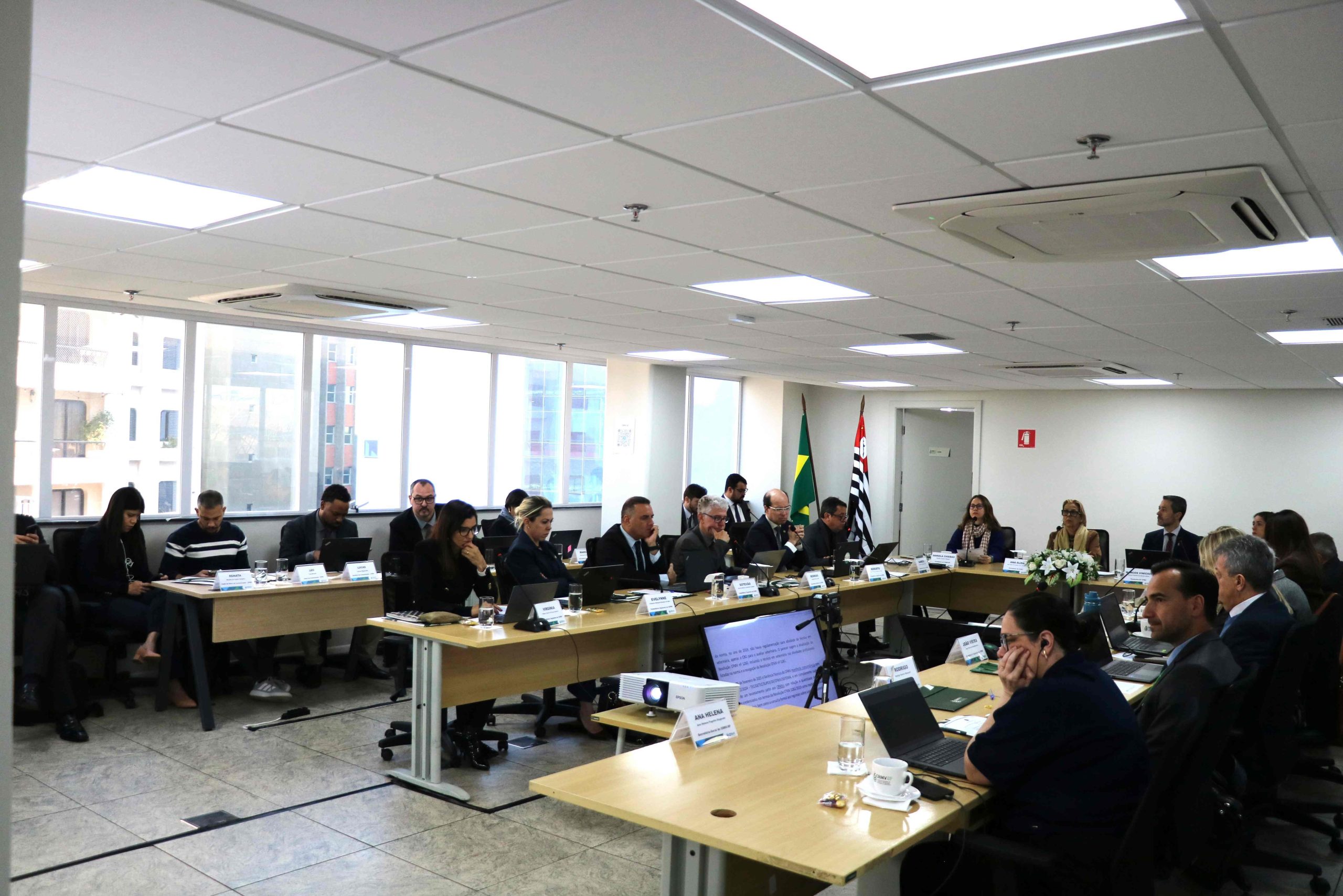 Pessoas sentadas a mesa assistindo ao telão.