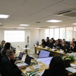 Pessoas sentadas a mesa assistindo ao telão.