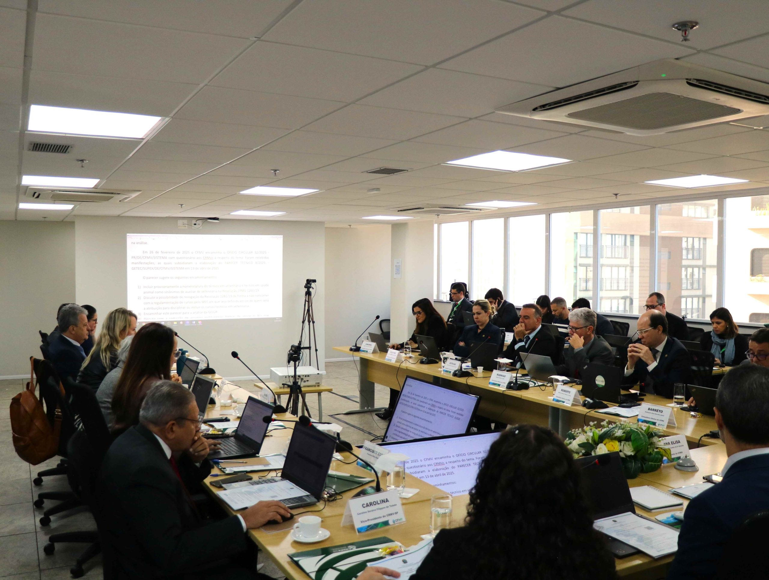 Pessoas sentadas a mesa assistindo ao telão.