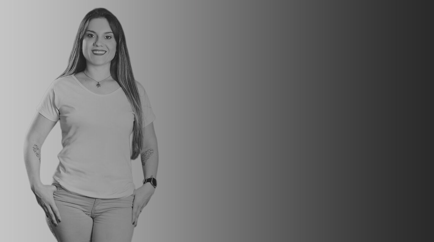 Mulher branca de cabelos lisos sorri para foto. Ela veste camiseta branca e calça jeans e está com as mãos nos bolsos da calça. No pulso esquerdo, ela usa um relógio. É a dra. Caroline Campagnone.