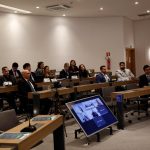 Pessoas sentadas à mesa frente ao palco.