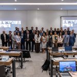 Pessoas em pé, pousando para foto, na frente de um palco em sala de treinamento no CFMV.