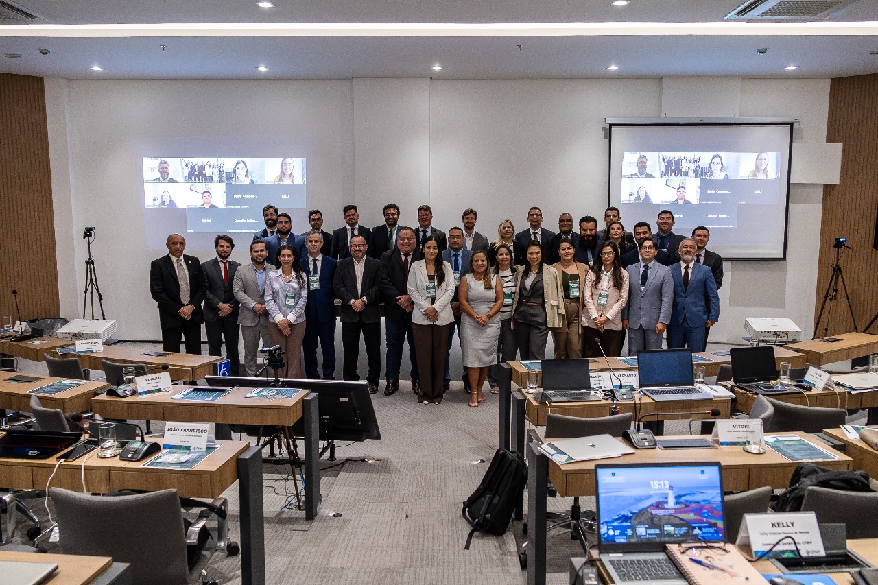 Pessoas em pé, pousando para foto, na frente de um palco em sala de treinamento no CFMV.