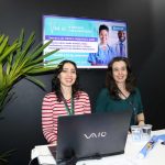 Mulheres juntas frente a um notebook posando para foto.