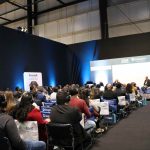 Pessoas sentadas de frente olhando para o telão.