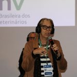 Mulher com fone de ouvido falando ao microfone. É a presidente do CFMV, Ana Elisa de Almeida.