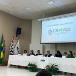 Pessoas sentadas a mesa a frente de telão.