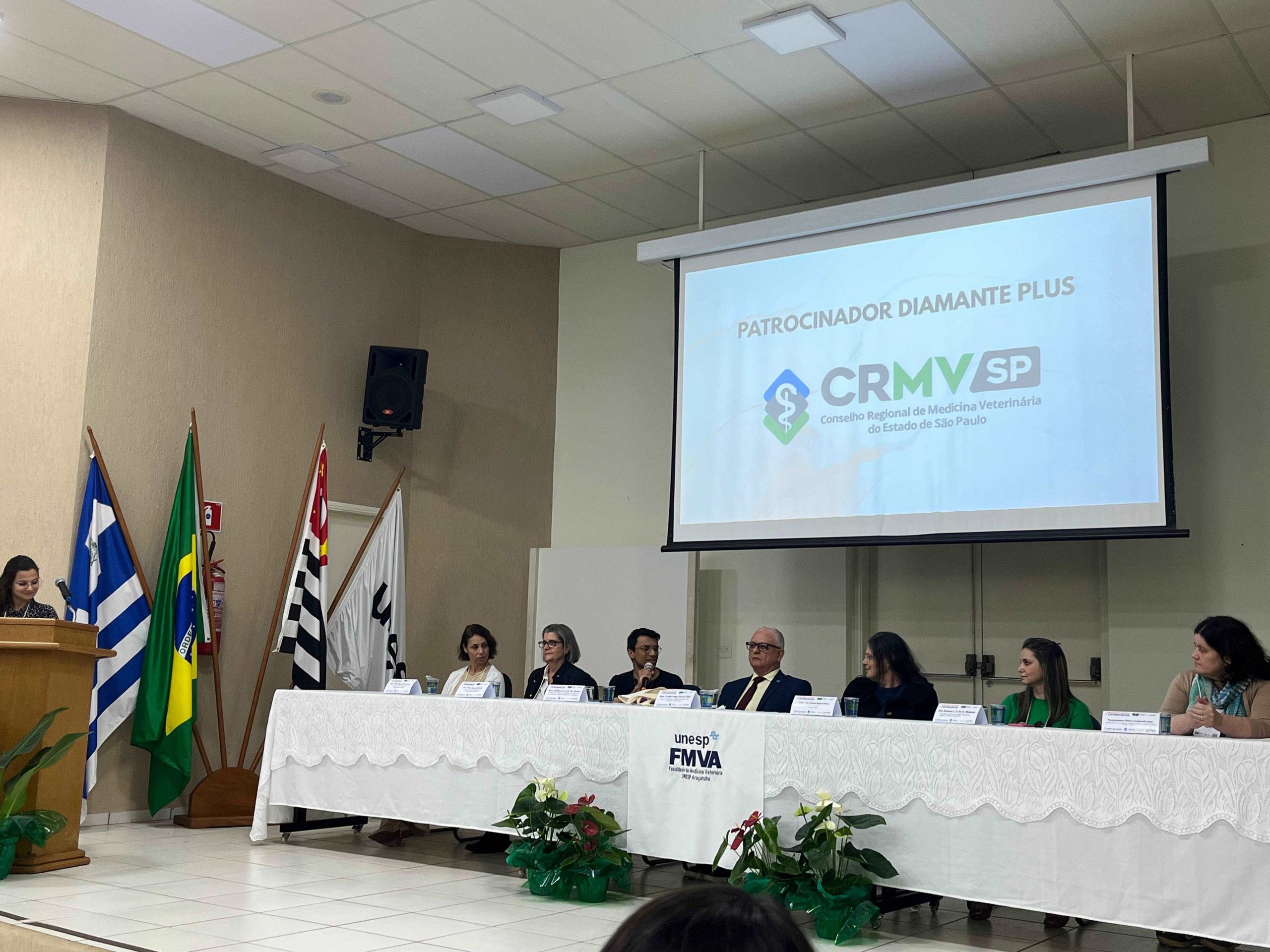 Pessoas sentadas a mesa a frente de telão.