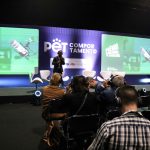 Homem em pé em cima de um palco, falando em microfone para plateia.