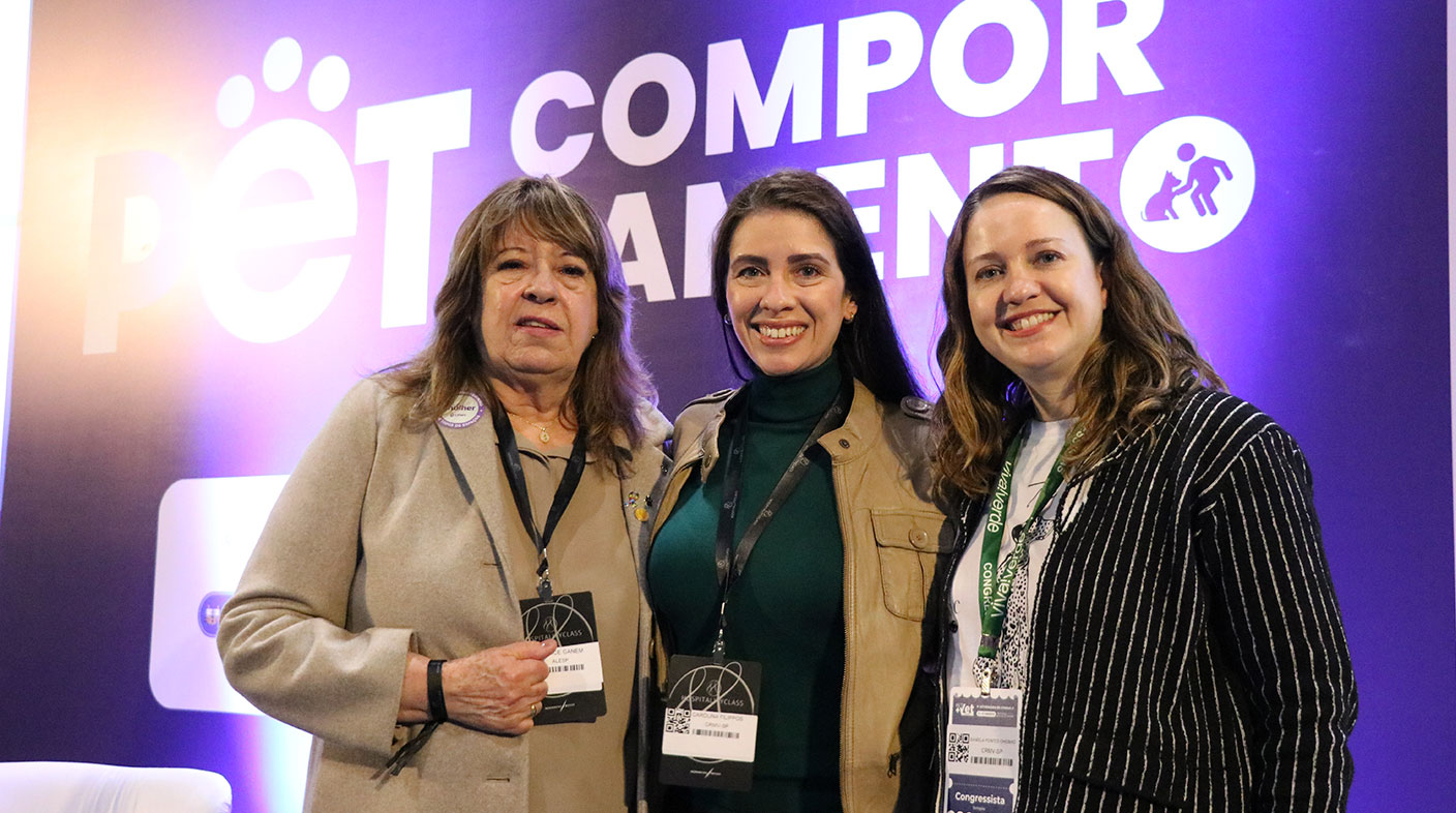 Três mulheres pousando para foto na frente de um painel roxo escrito Pet Comportamento em letras brancas. Da esquerda para a direita são elas: Deputada estadual Clarice Ganem, a vice-presidente do CRMV-SP Carolina Saraiva de Filippos e a presidente do CRMV-SP, Daniela Pontes Chiebao.
