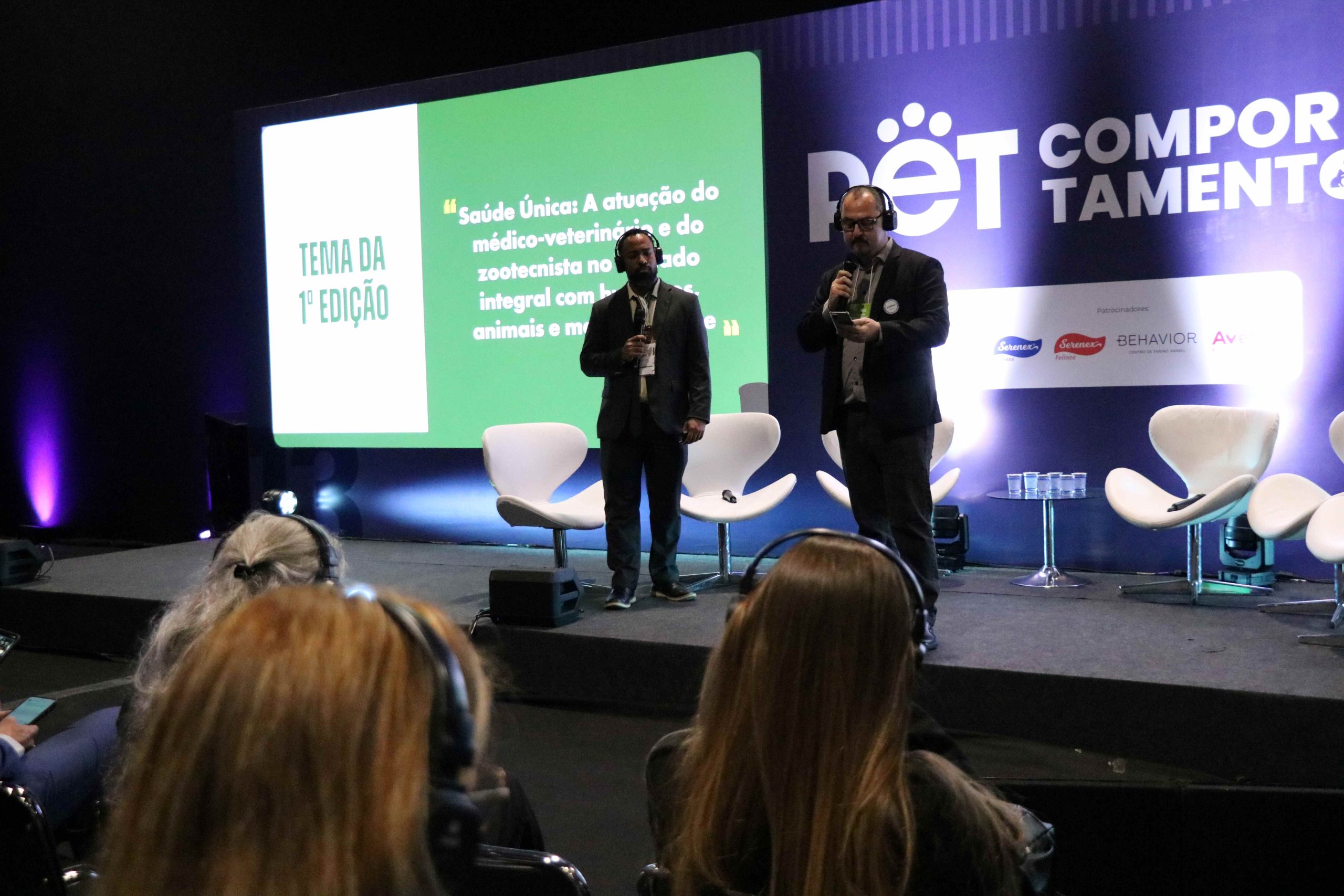 Dois homens em pé em cima do palco durante lançamento do Prêmio CFMV/CRMVs de Jornalismo.