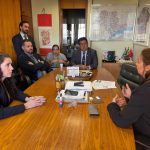 Cinco pessoas sentadas a mesa discutindo.