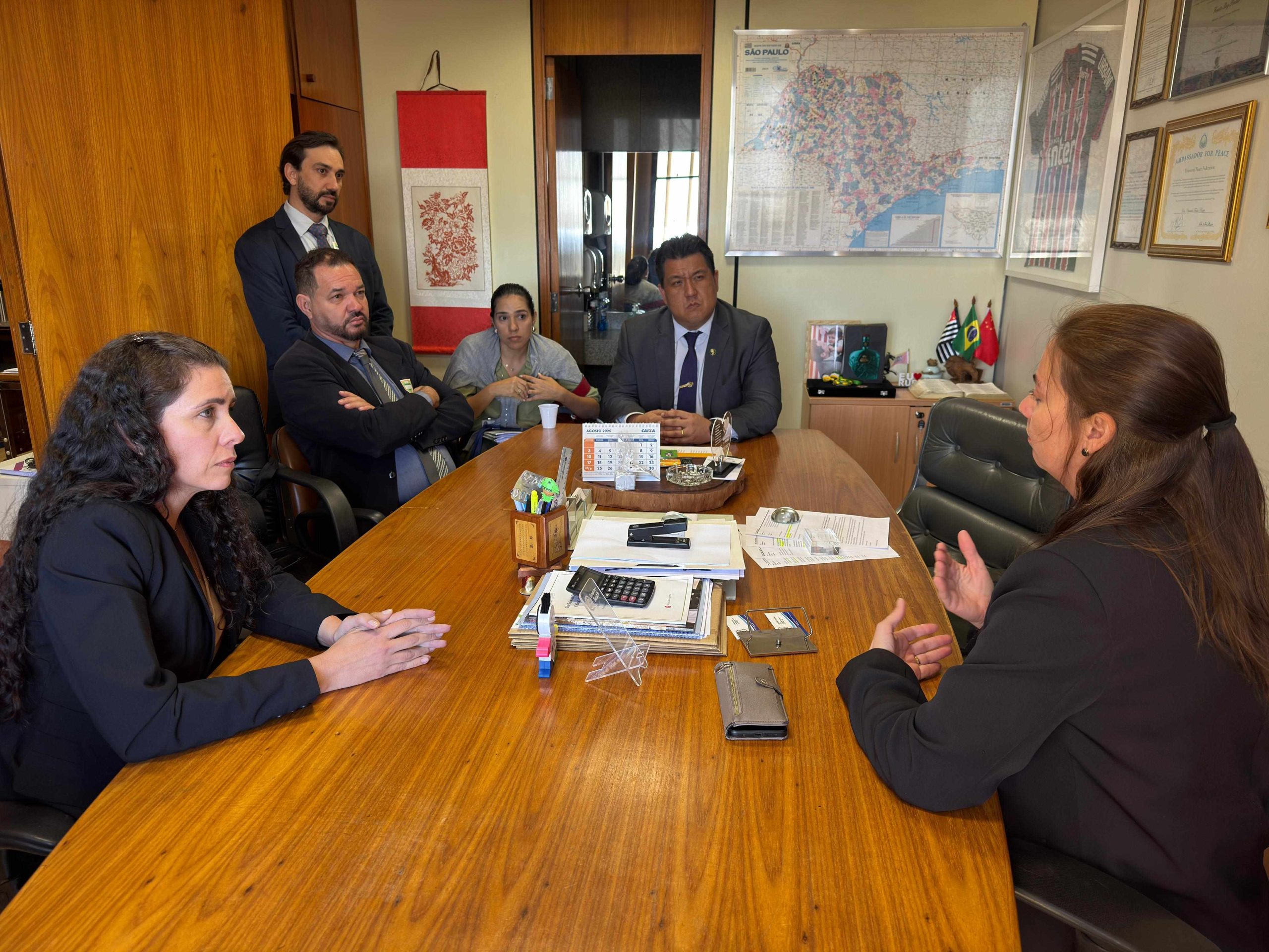 Cinco pessoas sentadas a mesa discutindo.