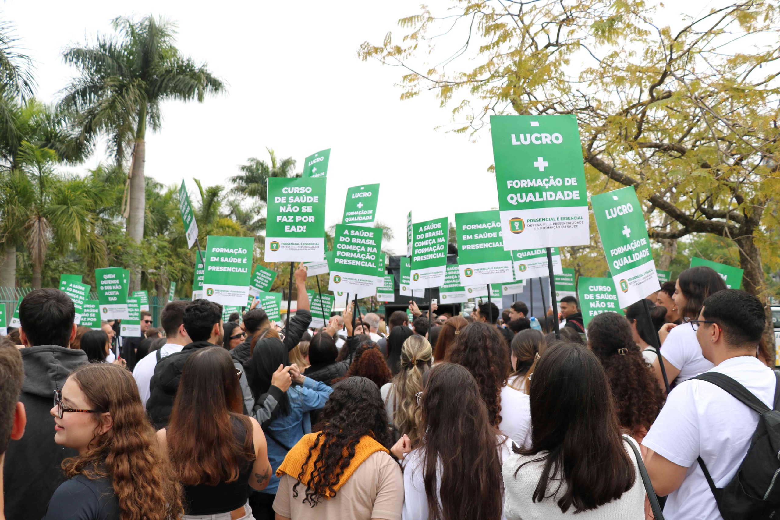 Pessoas com blusas brancas andando em passeata com placas em defesa do ensino presencial na área da Saúde.